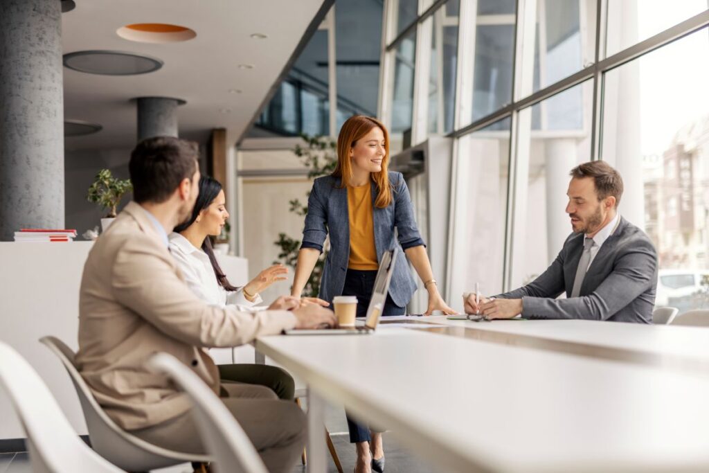 Team leader standing at the end of a meeting table with 3 other team members sitting around the table