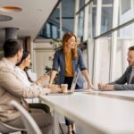 Team leader standing at the end of a meeting table with 3 other team members sitting around the table